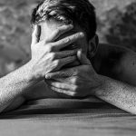 grayscale photo of man covering face with both hands