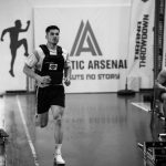 Male athlete running indoors during a competitive sports event with fitness branding.